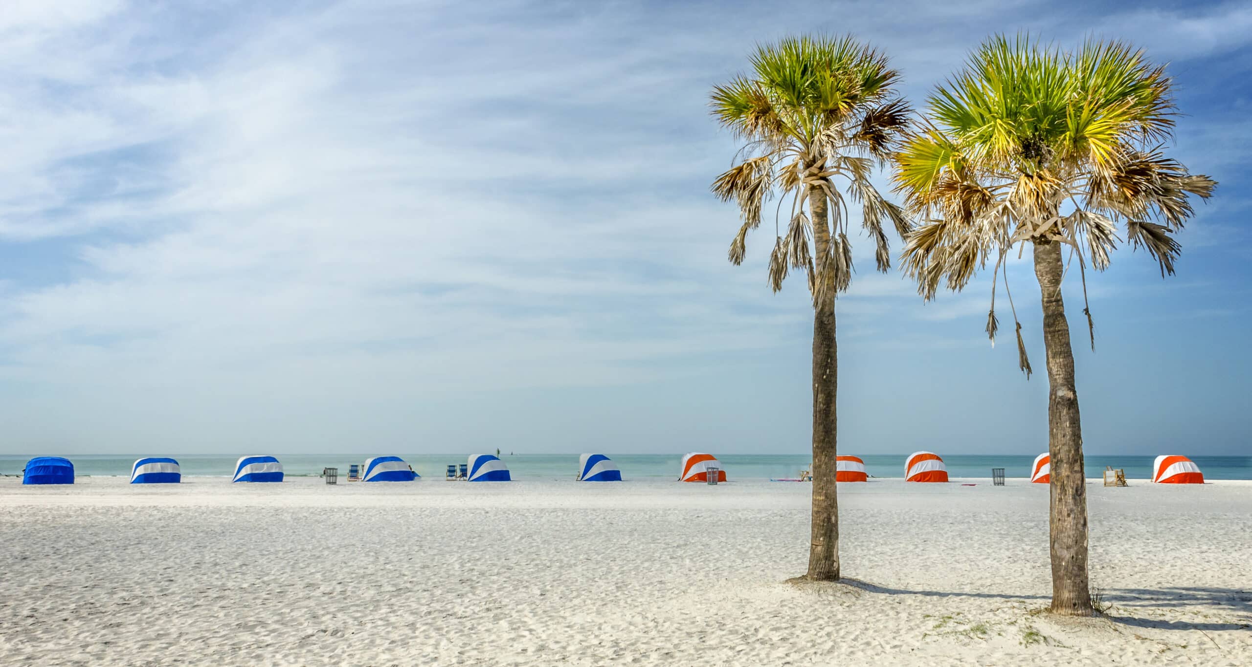 Two palm trees on white sand beach with striped beach cabanas on the edge of the beach in Clearwater, Florida one of the top destinations for best Florida resorts for couples